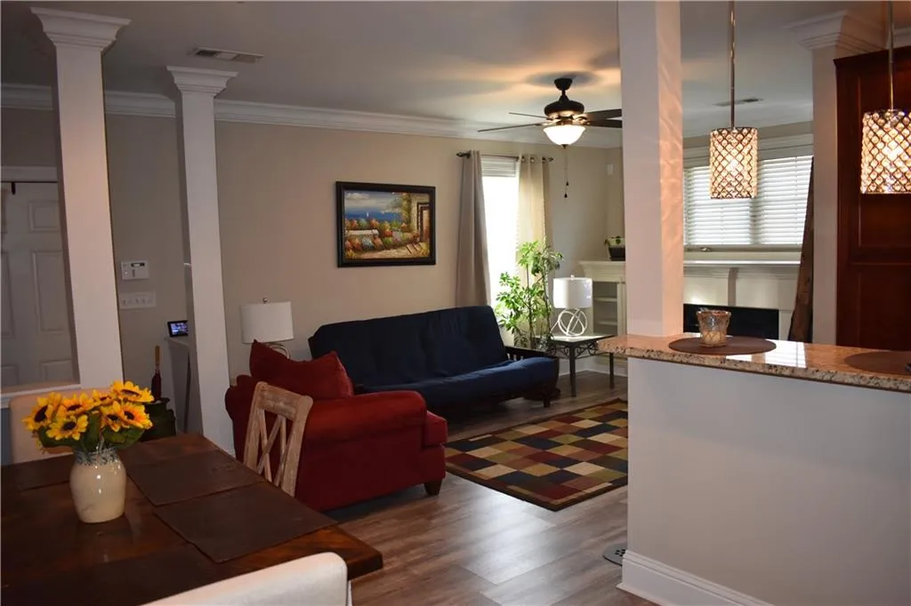 Living room featuring dark wood-type flooring, ceiling fan with notable chandelier, ornate columns, and crown molding