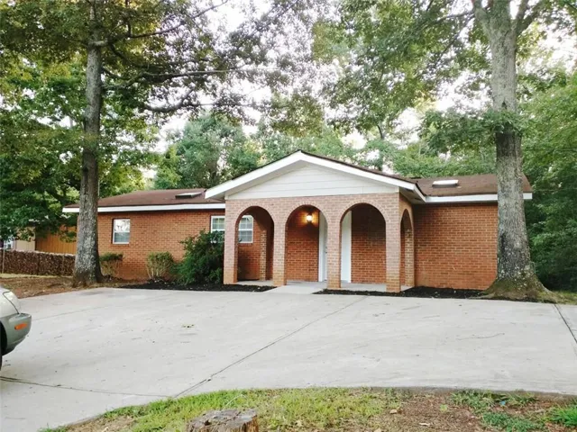 Brick exterior with an arched entryway, complemented by mature trees framing the property