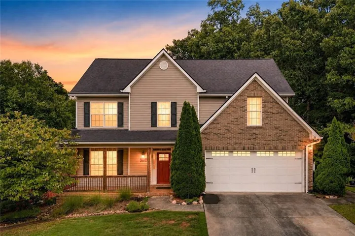 Traditional exterior featuring brick and siding accents, a covered front porch, an attached two-car garage, mature landscaping, and a red front door