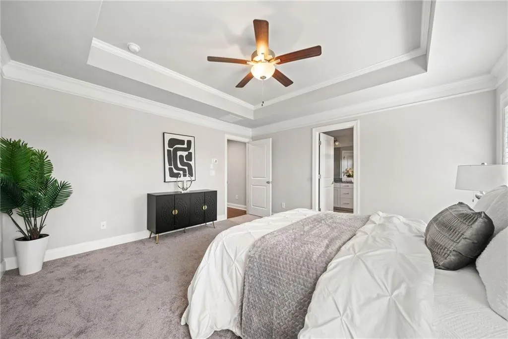 Bedroom featuring a raised ceiling, ornamental molding, carpet flooring, and ceiling fan
