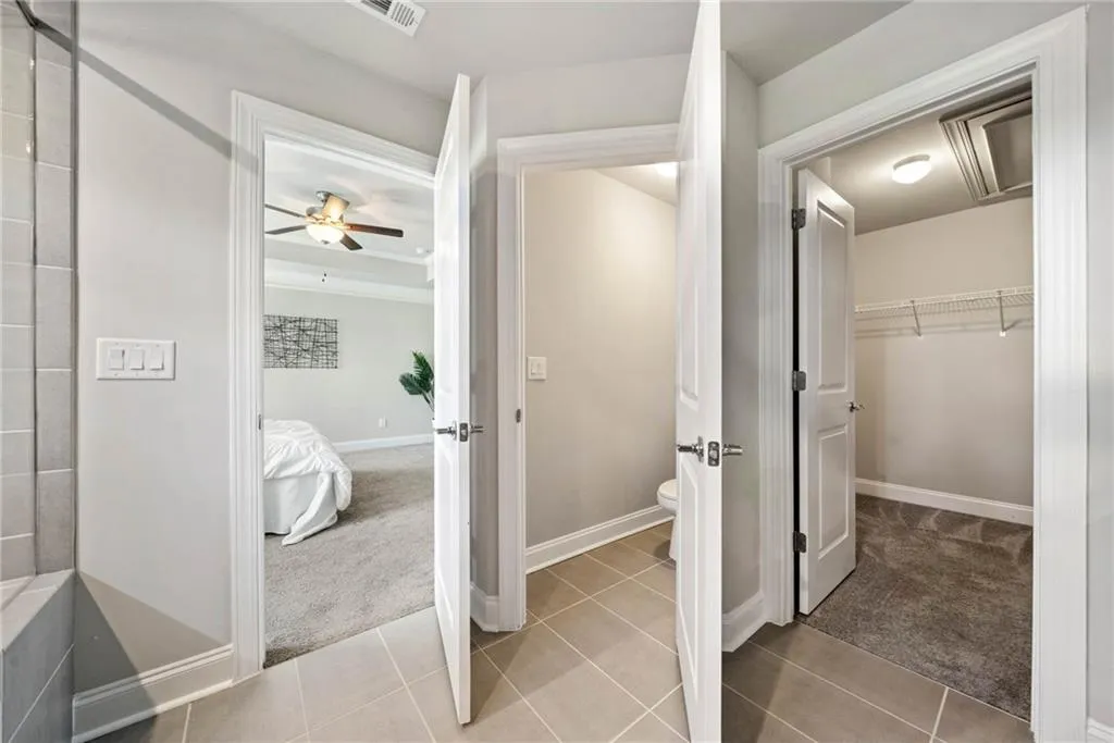 Ensuite bathroom featuring light tile patterned floors, a spacious closet, and a ceiling fan