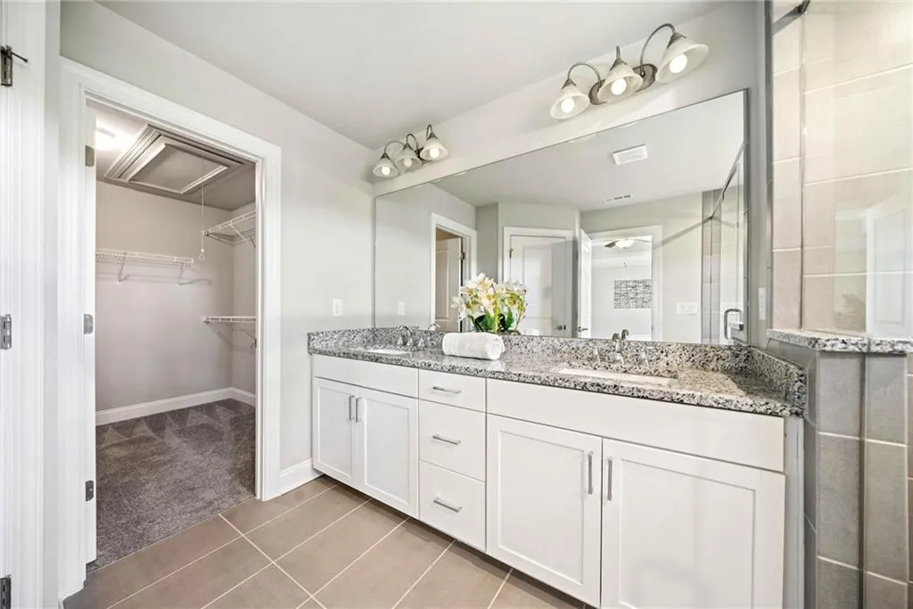 Full bath with light tile patterned flooring, double vanity, a stall shower, and a spacious closet