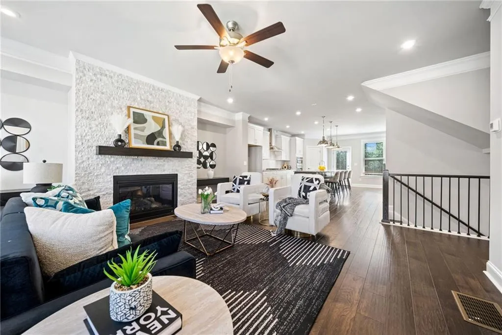 Living area with dark wood-style flooring, crown molding, a stone fireplace, recessed lighting, and ceiling fan
