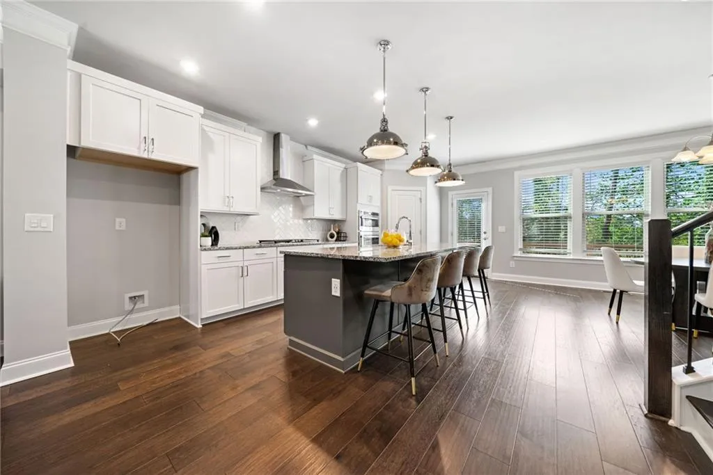 Kitchen with a breakfast bar area, white cabinets, decorative light fixtures, light stone counters, and backsplash