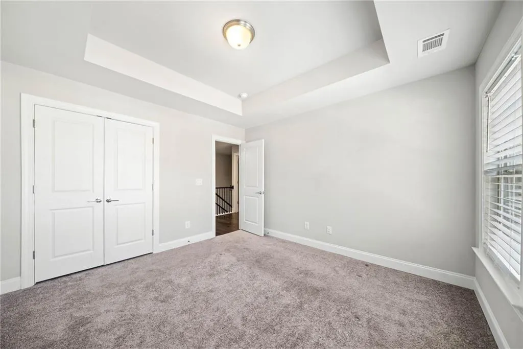 Unfurnished bedroom with carpet floors, a tray ceiling, and a closet