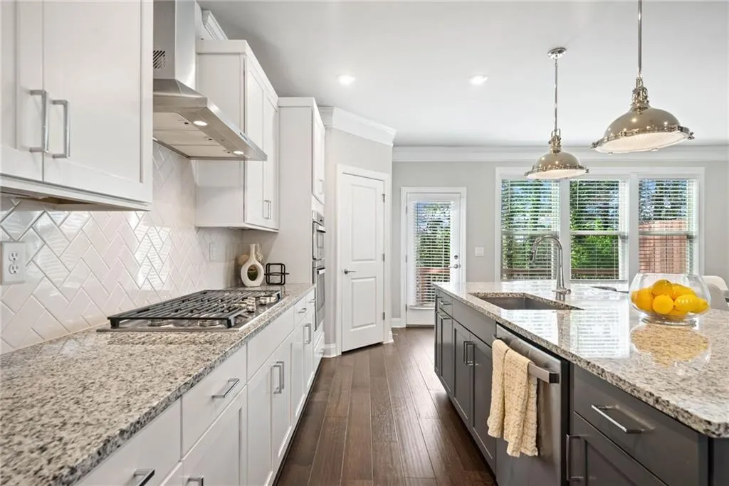 Kitchen with white cabinetry, light stone countertops, pendant lighting, wall chimney range hood, and ornamental molding