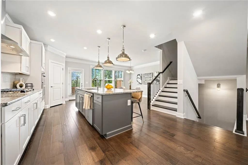 Kitchen featuring white cabinets, light stone countertops, a kitchen breakfast bar, hanging light fixtures, and a center island with sink