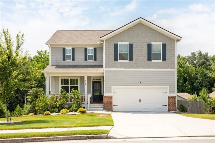 Two-story residence featuring light gray siding, dark shutters, a covered porch with white railing, a two-car garage, and a concrete driveway