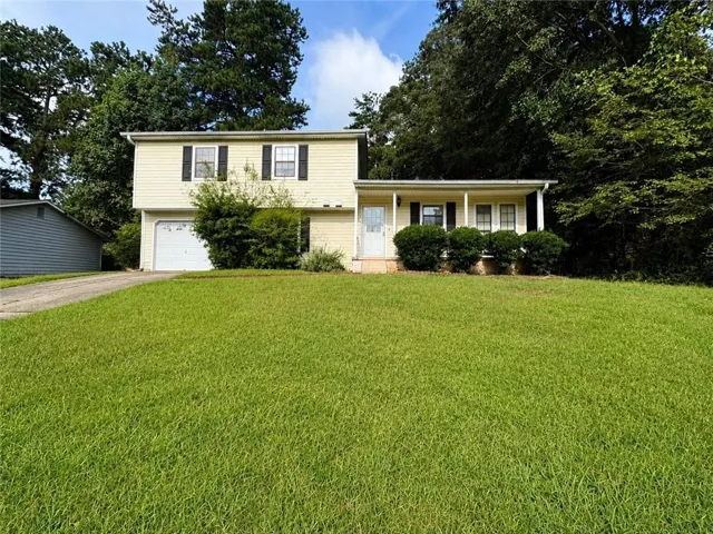 Charming two-story residence featuring a cream-colored exterior with black shutters, front-load garage, and expansive manicured lawn bordered by mature landscaping