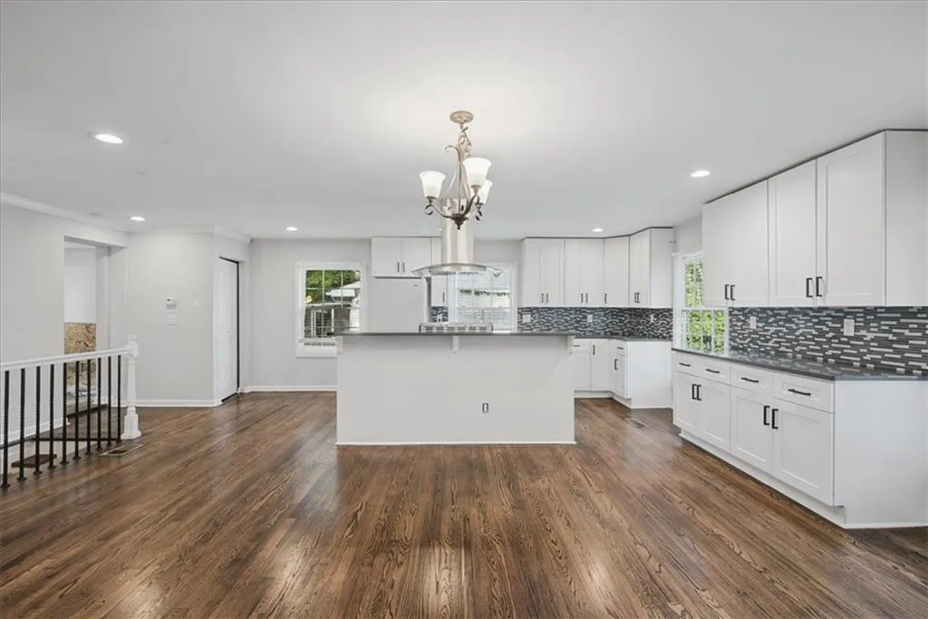 Open-concept kitchen featuring wood-finish flooring, white cabinetry, dark countertops, a tiled backsplash, and a central island with a breakfast bar