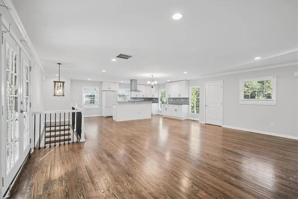 Expansive wood-finish flooring, recessed lighting, white kitchen cabinetry, stainless steel range hood, and a kitchen island