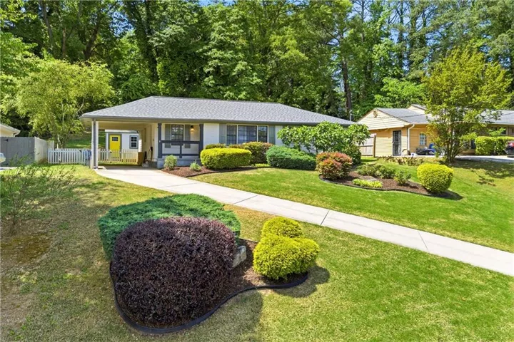 Ranch-style residence featuring a carport, front yard with mature landscaping, and an asphalt shingle roof