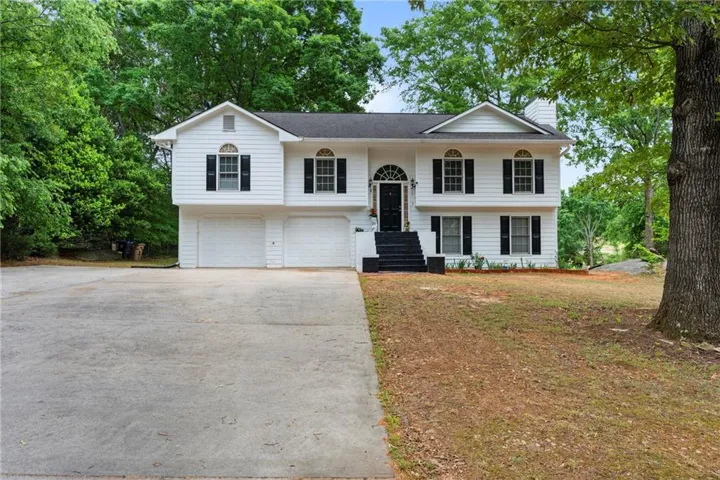 Split-level home featuring a white siding exterior with black shutters and a prominent front entry with an arched transom window