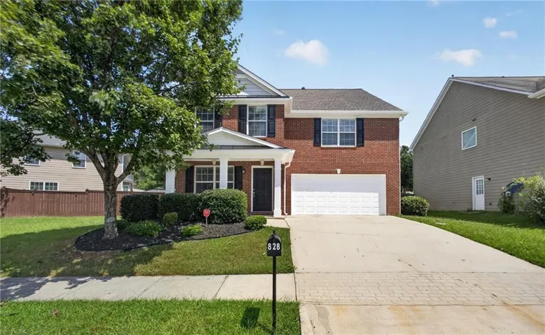 Two-story brick facade with white trim, a covered porch entry, an attached garage, and a concrete driveway