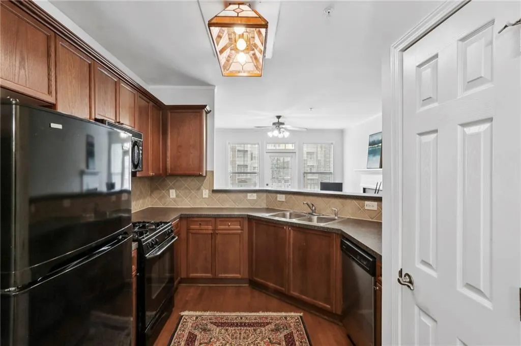 Kitchen with black appliances, dark wood finished floors, dark countertops, and tasteful backsplash and pantry.
