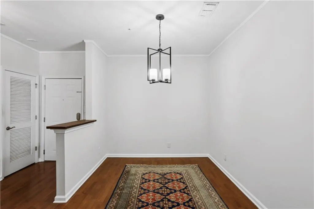 Unfurnished dining area featuring dark wood-style flooring, crown molding, and a chandelier