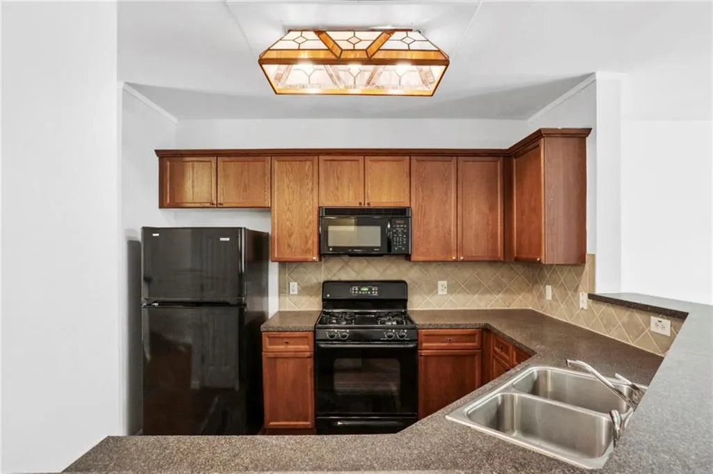 Kitchen featuring tasteful backsplash, black appliances, dark countertops, brown cabinets, and ornamental molding
