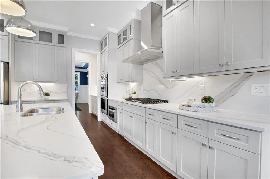 Kitchen featuring wall chimney exhaust hood, ornamental molding, tasteful backsplash, dark wood finished floors, and light stone countertops