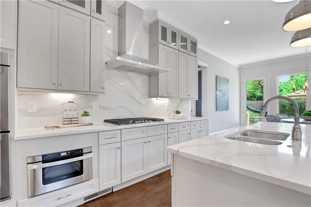 Kitchen with wall chimney range hood, dark wood finished floors, crown molding, tasteful backsplash, and glass insert cabinets