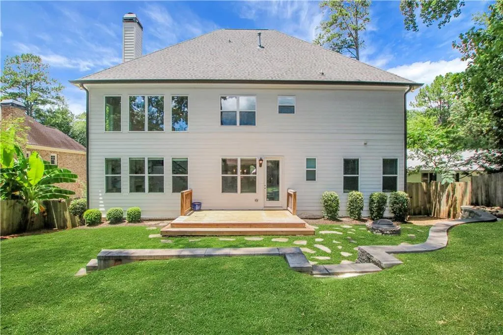 Back of house featuring a deck, a fire pit, roof with shingles, and a chimney