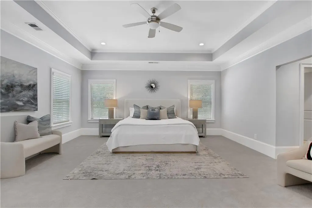 Bedroom featuring a tray ceiling, carpet floors, multiple windows, ornamental molding, and recessed lighting