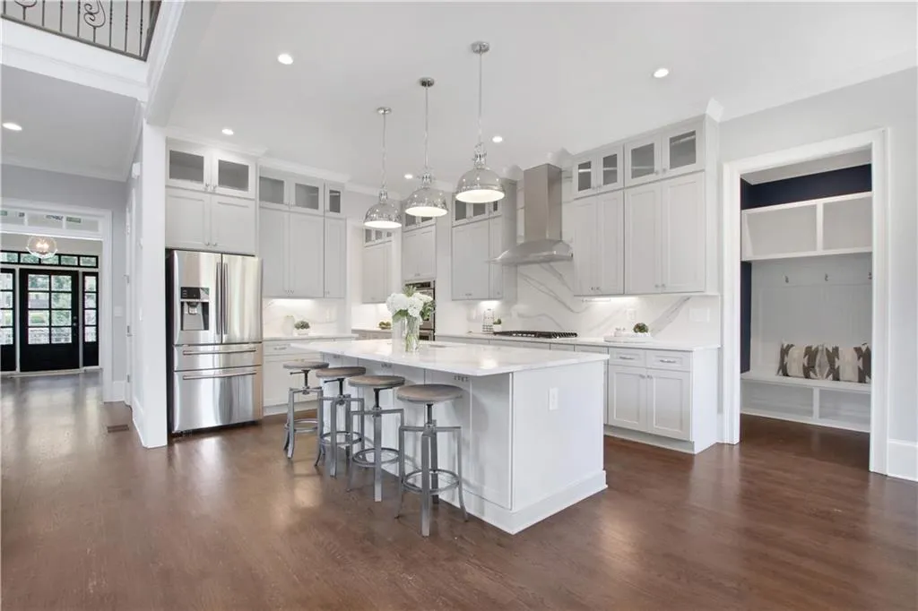 Kitchen with stainless steel refrigerator with ice dispenser, light countertops, a center island with sink, wall chimney range hood, and dark wood-style flooring