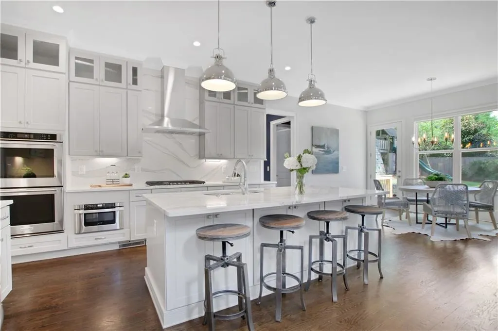Kitchen featuring stainless steel double oven, wall chimney range hood, dark wood-style floors, a kitchen island with sink, and a kitchen bar