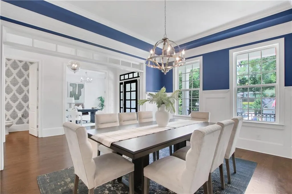 Dining area with a chandelier, dark wood-type flooring, a wainscoted wall, ornamental molding, and a decorative wall