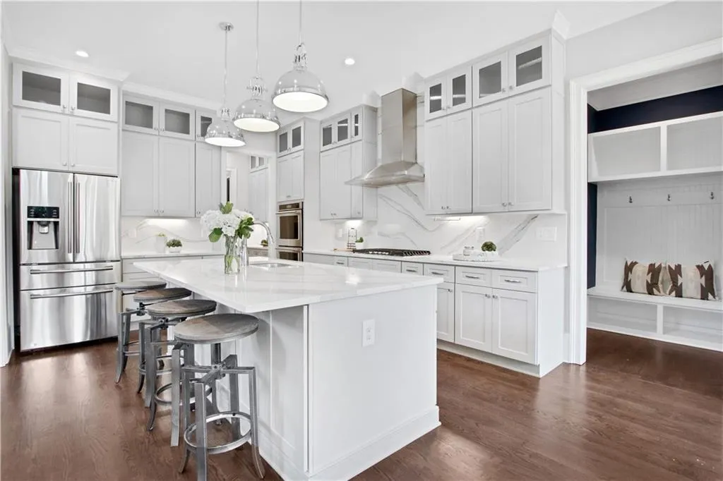Kitchen featuring appliances with stainless steel finishes, wall chimney exhaust hood, a kitchen island with sink, a kitchen breakfast bar, and dark wood-style floors