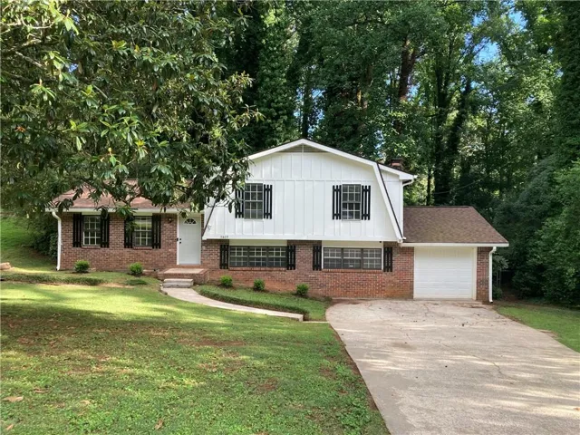 Split-level residence featuring a brick and white vertical siding exterior, a white garage door, and a concrete driveway