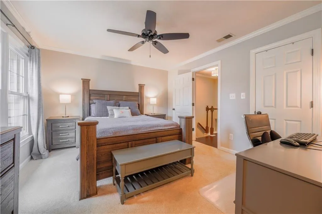 Bedroom with light carpet, ornamental molding, ceiling fan, and an office area