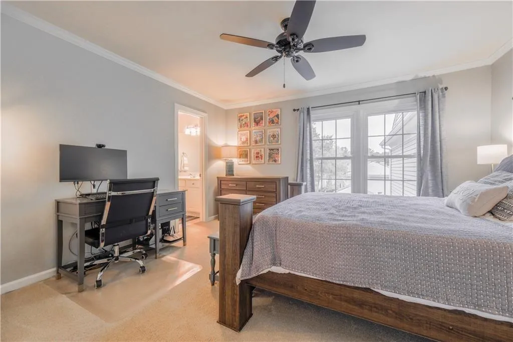 Bedroom with crown molding, light colored carpet, an office area, a ceiling fan, and ensuite bath