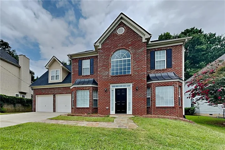 Red brick exterior featuring a multi-level design, a two-car garage, a stone walkway, a prominent arched window, and decorative shutters