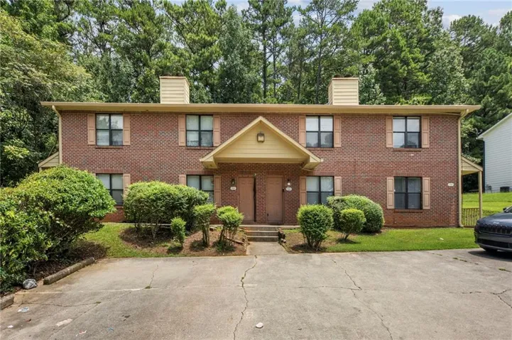 Two-story brick exterior featuring a central covered entry, tan shutters, and two prominent chimneys