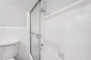 Bathroom with a shower with shower door, toilet, and tile walls