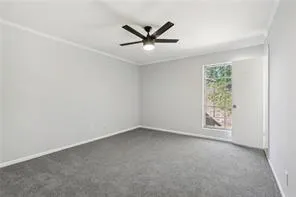 Empty room with baseboards, dark carpet, crown molding, and ceiling fan