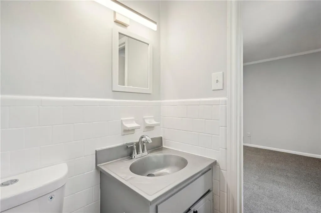 Half bath featuring vanity, tile walls, a wainscoted wall, and crown molding