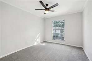 Carpeted empty room featuring crown molding, baseboards, and a ceiling fan