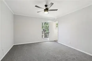 Carpeted spare room featuring baseboards, ceiling fan, and crown molding