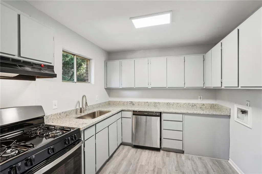 Kitchen featuring gas range, stainless steel dishwasher, under cabinet range hood, light wood finished floors, and light stone countertops