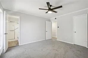 Unfurnished bedroom featuring carpet flooring, ensuite bath, baseboards, crown molding, and a ceiling fan