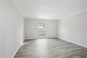 Unfurnished room featuring wood finished floors, crown molding, and baseboards