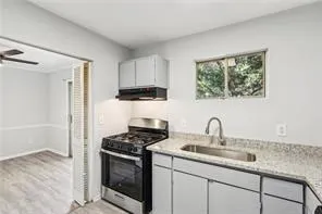 Kitchen with stainless steel gas range oven, ventilation hood, a sink, light wood-style floors, and white cabinetry