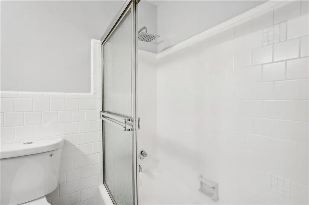 Bathroom featuring tile walls, shower / bath combination with glass door, and wainscoting