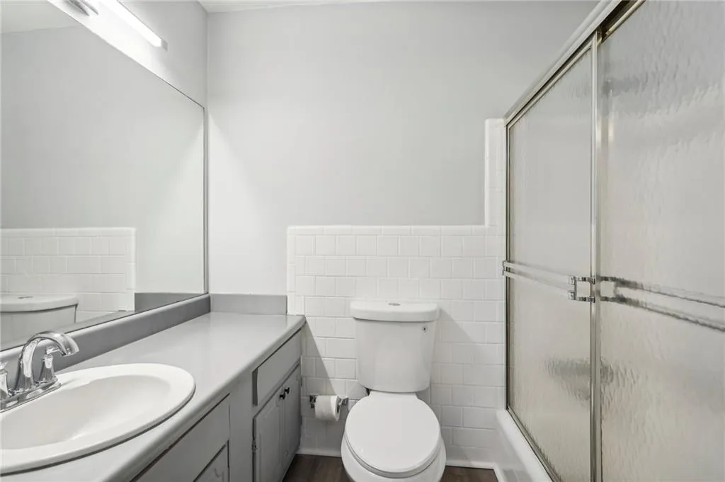 Bathroom featuring tile walls, vanity, enclosed tub / shower combo, and wainscoting