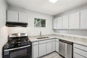 Kitchen with stainless steel appliances, under cabinet range hood, a sink, and light countertops