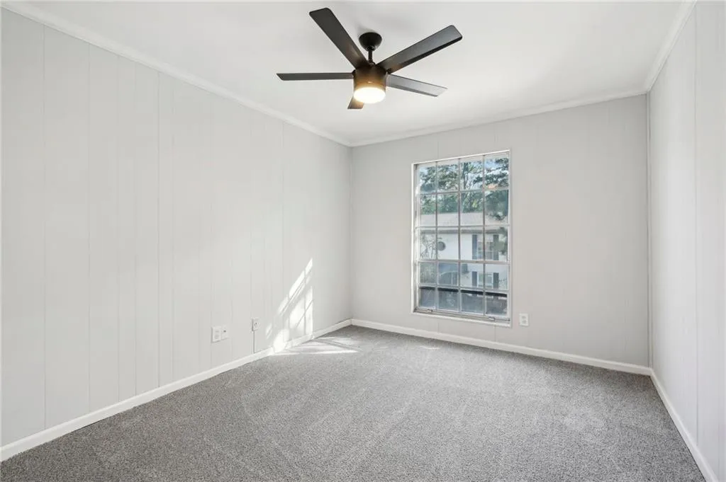 Carpeted empty room with crown molding, ceiling fan, and wooden walls