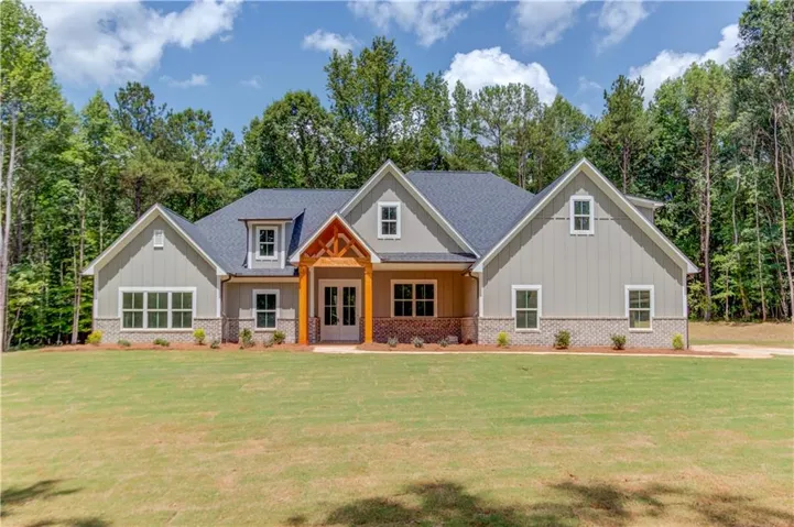 Contemporary craftsman-style residence featuring a prominent front gable, light gray board-and-batten siding, a dark shingle roof, and a stone veneer foundation