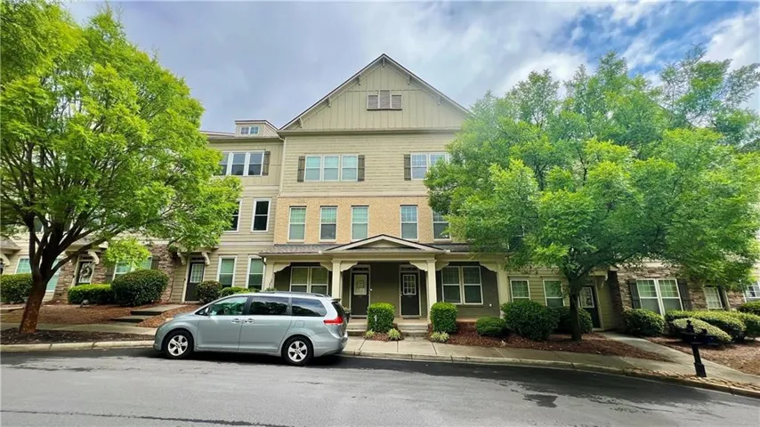 Multi-level townhome featuring a neutral-toned facade with stone accents, covered entry porch, and dark shutters