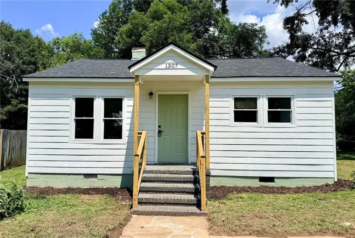 White siding exterior with a dark shingle roof, featuring a light green entry door, covered porch, and wood railings